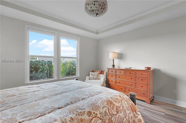 bedroom featuring crown molding, a raised ceiling, and light wood-type flooring