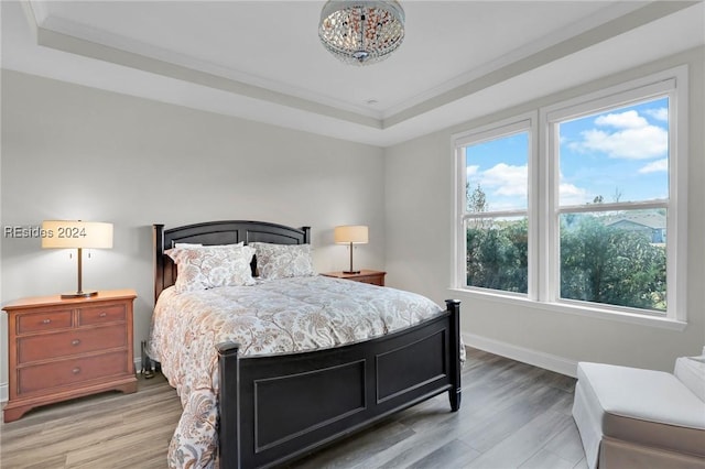 bedroom with crown molding, light wood-type flooring, and a tray ceiling