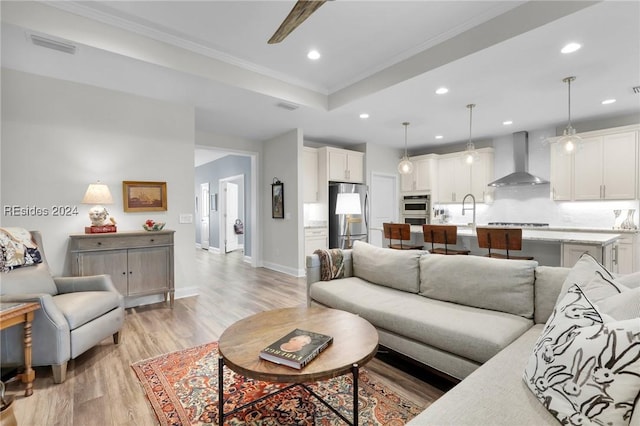 living room featuring sink, ceiling fan, a tray ceiling, ornamental molding, and light hardwood / wood-style floors