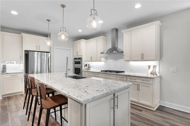 kitchen with decorative light fixtures, tasteful backsplash, wall chimney range hood, stainless steel appliances, and a center island with sink