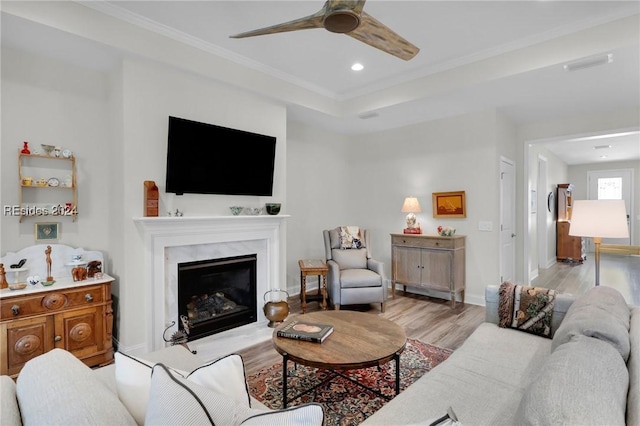 living room with ceiling fan, ornamental molding, a premium fireplace, and light hardwood / wood-style flooring