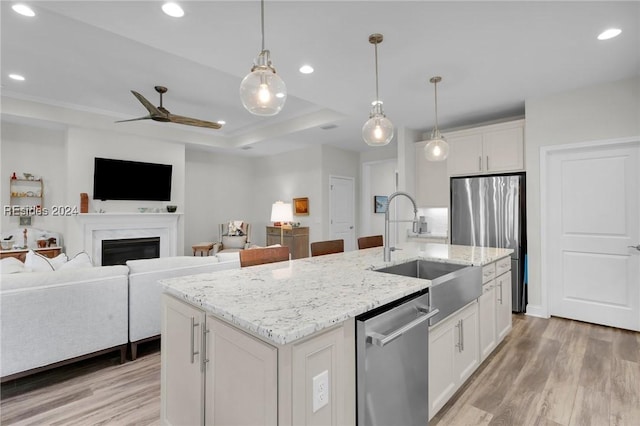 kitchen featuring sink, an island with sink, pendant lighting, stainless steel appliances, and white cabinets