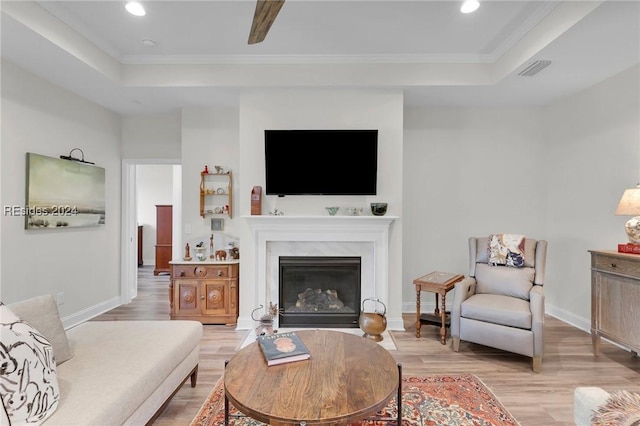 living room featuring crown molding, a raised ceiling, and light hardwood / wood-style floors