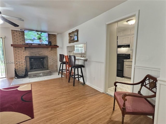 living room with a brick fireplace, plenty of natural light, light hardwood / wood-style floors, and ceiling fan