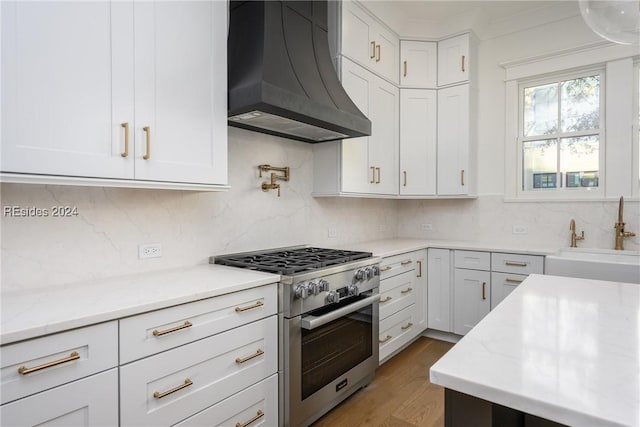 kitchen with white cabinetry, high end range, custom range hood, and backsplash