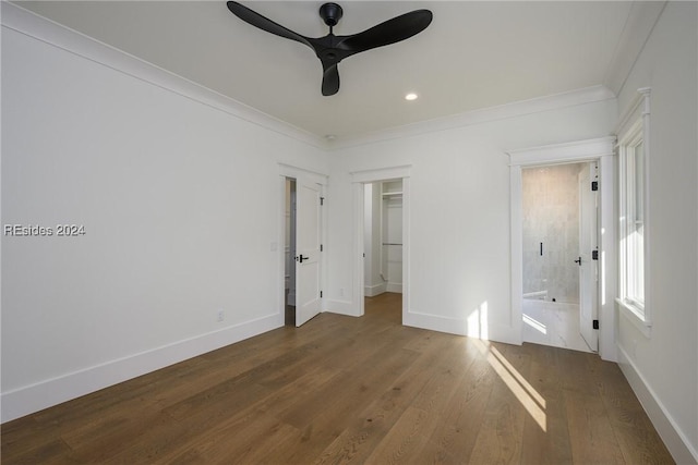 unfurnished bedroom with crown molding, ensuite bath, ceiling fan, hardwood / wood-style floors, and a spacious closet