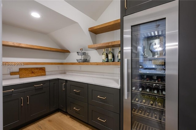 bar with beverage cooler, vaulted ceiling, and light hardwood / wood-style flooring