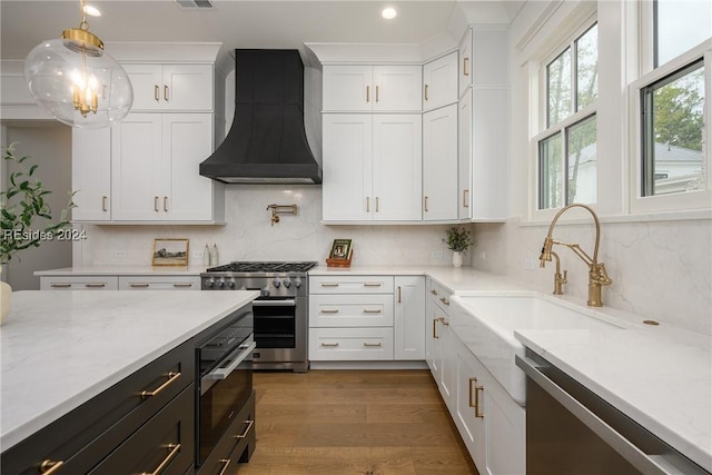 kitchen with appliances with stainless steel finishes, tasteful backsplash, white cabinets, custom exhaust hood, and hanging light fixtures