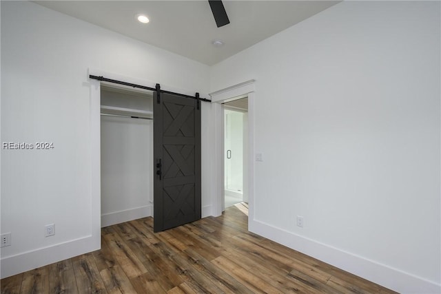 unfurnished bedroom with a barn door, dark hardwood / wood-style floors, and ceiling fan