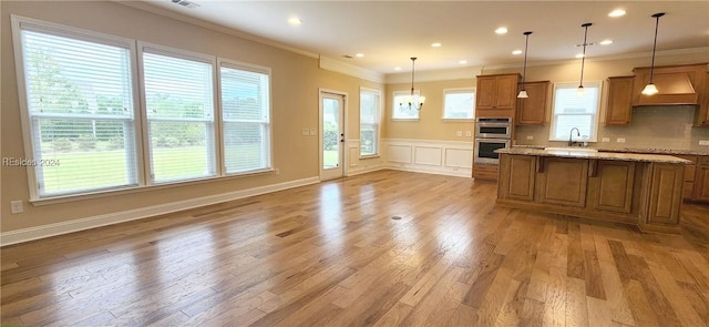 kitchen featuring decorative light fixtures, light hardwood / wood-style floors, light stone counters, crown molding, and a healthy amount of sunlight