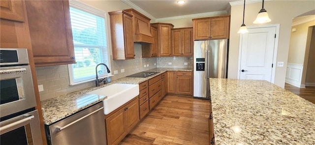 kitchen with stainless steel appliances, hanging light fixtures, sink, and light stone counters