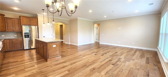 kitchen with a kitchen island, decorative light fixtures, stainless steel fridge, backsplash, and light stone countertops