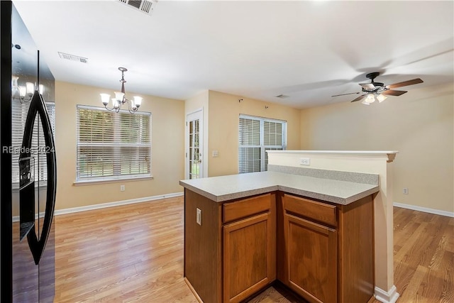 kitchen featuring ceiling fan with notable chandelier, a center island, decorative light fixtures, black refrigerator with ice dispenser, and light wood-type flooring