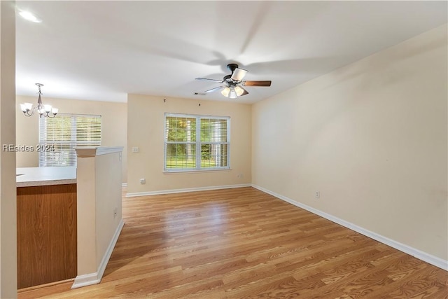 spare room featuring ceiling fan with notable chandelier and light wood-type flooring