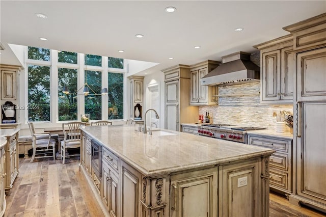 kitchen featuring stainless steel gas stovetop, sink, a kitchen island with sink, light stone countertops, and wall chimney range hood