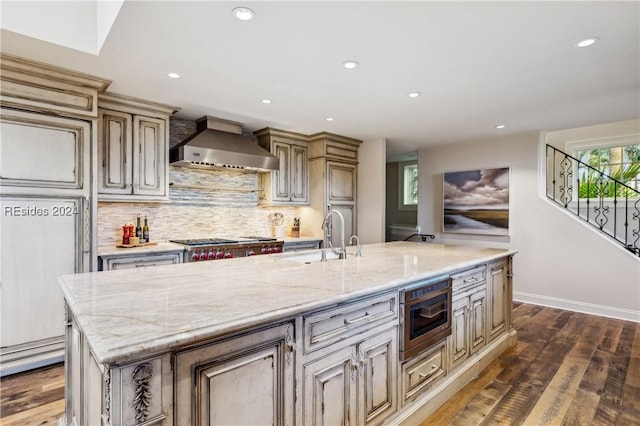 kitchen featuring sink, light stone countertops, an island with sink, and wall chimney exhaust hood