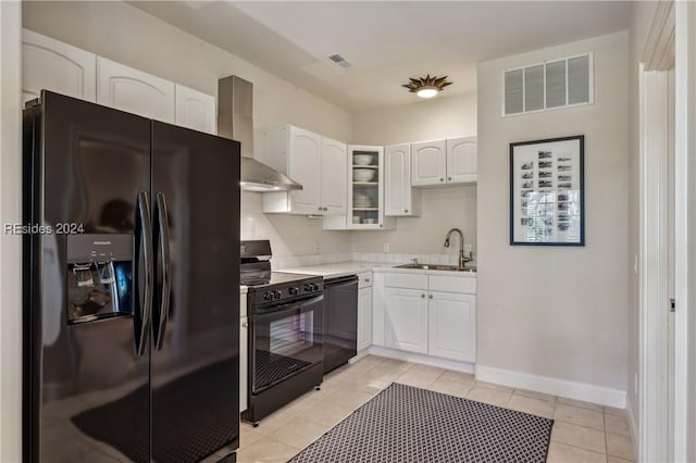 kitchen with light tile patterned flooring, sink, white cabinetry, black appliances, and wall chimney range hood