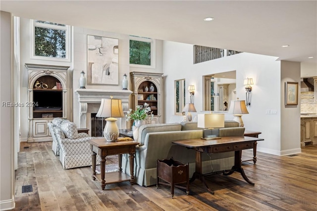 living room with a towering ceiling, wood-type flooring, and built in shelves