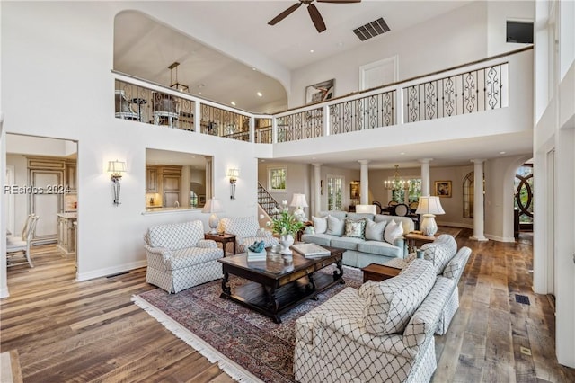 living room featuring ceiling fan with notable chandelier, wood-type flooring, decorative columns, and a high ceiling