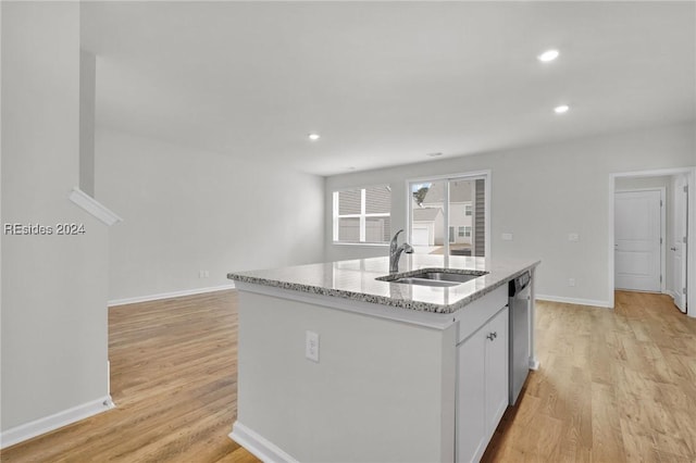 kitchen with sink, a kitchen island with sink, white cabinets, stainless steel dishwasher, and light wood-type flooring