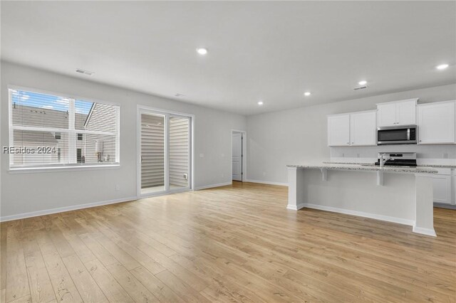 kitchen featuring appliances with stainless steel finishes, an island with sink, a breakfast bar area, white cabinets, and light stone countertops