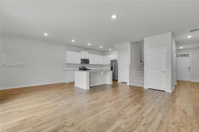 kitchen with a kitchen island with sink, white cabinetry, stainless steel appliances, light hardwood / wood-style floors, and a kitchen bar