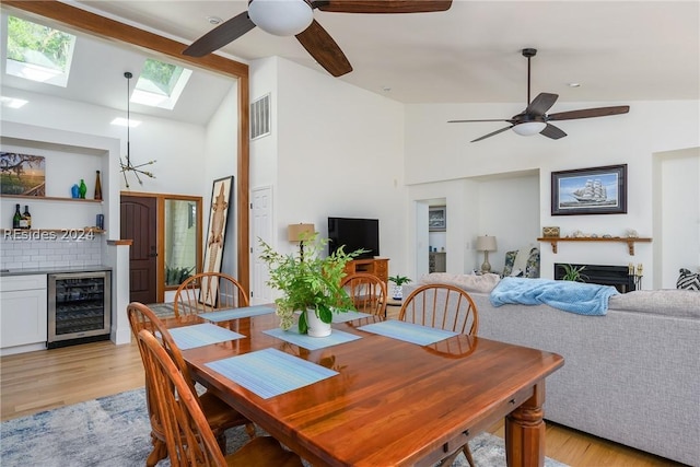 dining room featuring lofted ceiling with skylight, wine cooler, ceiling fan, and light hardwood / wood-style flooring