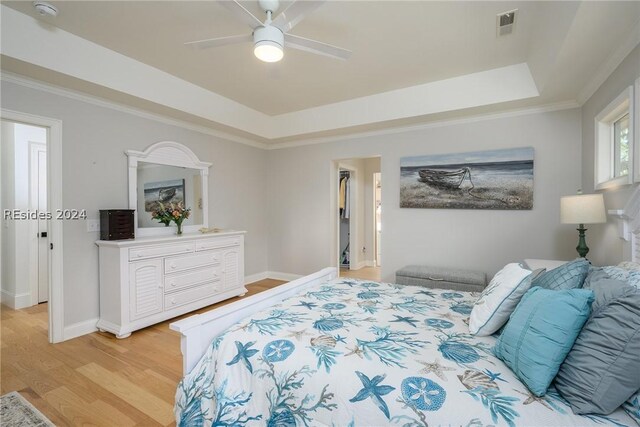 bedroom featuring crown molding, light hardwood / wood-style flooring, a raised ceiling, and ceiling fan