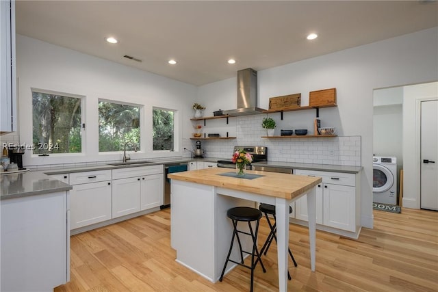 kitchen with wood counters, wall chimney exhaust hood, washer / dryer, white cabinetry, and stainless steel range with electric stovetop