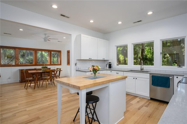 kitchen featuring sink, butcher block countertops, dishwasher, white cabinetry, and a center island