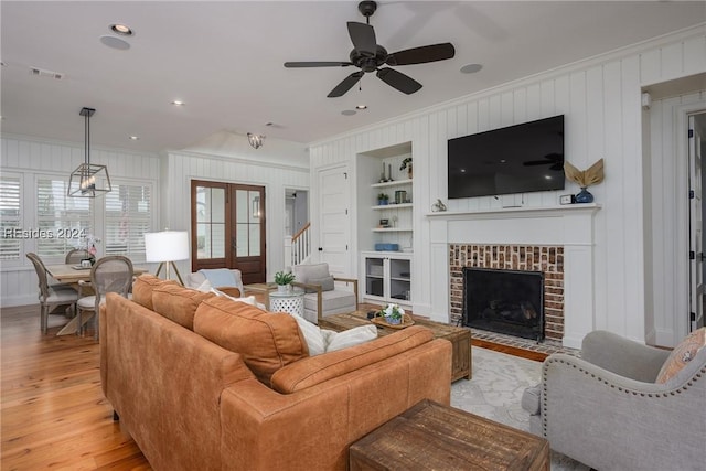 living room with light hardwood / wood-style flooring, built in features, ceiling fan, a fireplace, and french doors