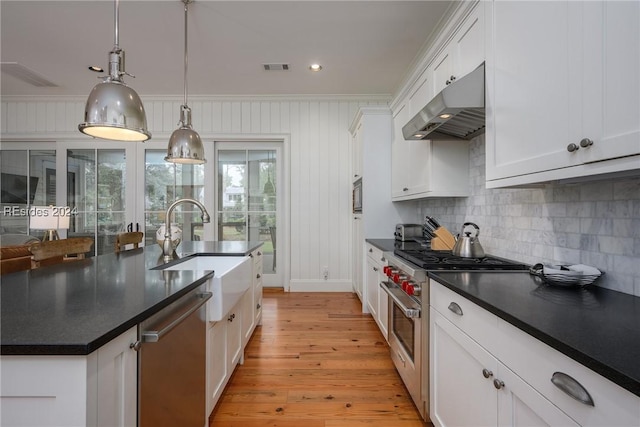 kitchen featuring appliances with stainless steel finishes, decorative light fixtures, white cabinetry, an island with sink, and light hardwood / wood-style floors