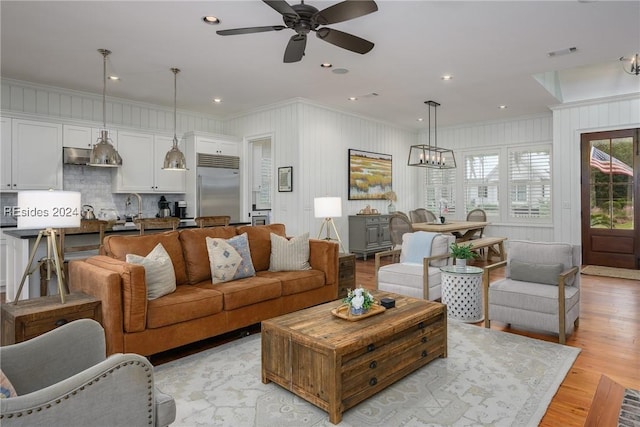 living room with ornamental molding, ceiling fan with notable chandelier, and light hardwood / wood-style flooring