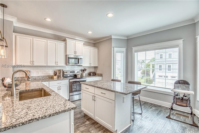 kitchen featuring sink, stainless steel appliances, light stone countertops, white cabinets, and a kitchen island