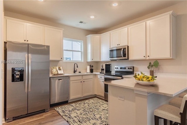 kitchen featuring stainless steel appliances, sink, white cabinets, and a kitchen bar