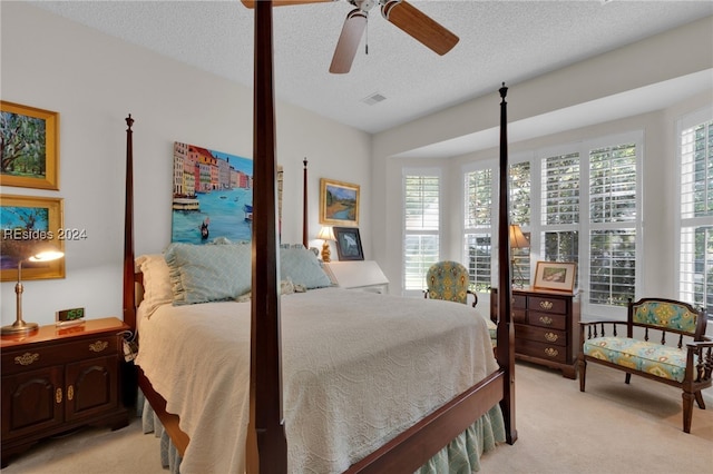 bedroom with a textured ceiling, light colored carpet, and ceiling fan