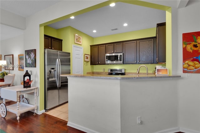 kitchen featuring appliances with stainless steel finishes, light wood-type flooring, dark brown cabinetry, and kitchen peninsula