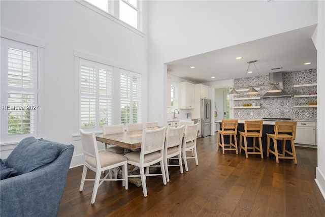 dining room featuring a healthy amount of sunlight, dark hardwood / wood-style flooring, and a high ceiling