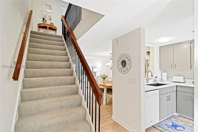 stairway with an inviting chandelier, sink, and hardwood / wood-style flooring