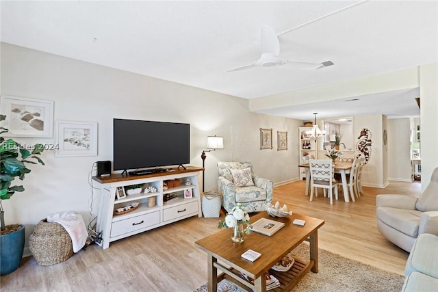 living room featuring ceiling fan with notable chandelier and light hardwood / wood-style flooring