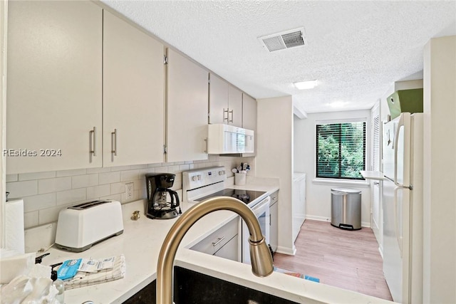 kitchen featuring backsplash, a textured ceiling, white appliances, and light hardwood / wood-style floors