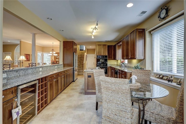 kitchen with high quality fridge, kitchen peninsula, double oven, beverage cooler, and light stone countertops