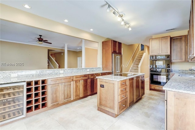 kitchen with wine cooler, sink, light stone counters, a center island, and black appliances