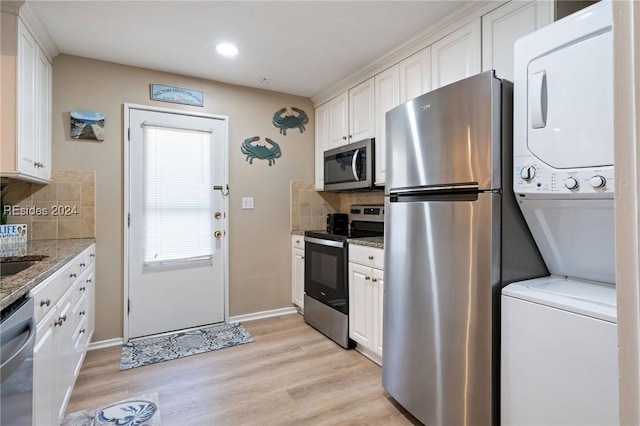 kitchen with stacked washer and dryer, appliances with stainless steel finishes, white cabinetry, backsplash, and light stone countertops