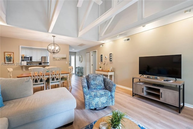 living room featuring high vaulted ceiling, light hardwood / wood-style floors, and a chandelier