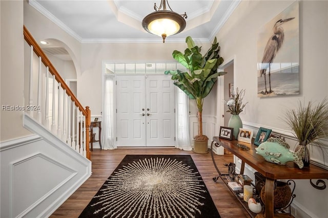 entrance foyer featuring a raised ceiling, ornamental molding, and dark hardwood / wood-style flooring