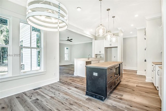 kitchen with hanging light fixtures, white cabinetry, a center island, and light hardwood / wood-style floors