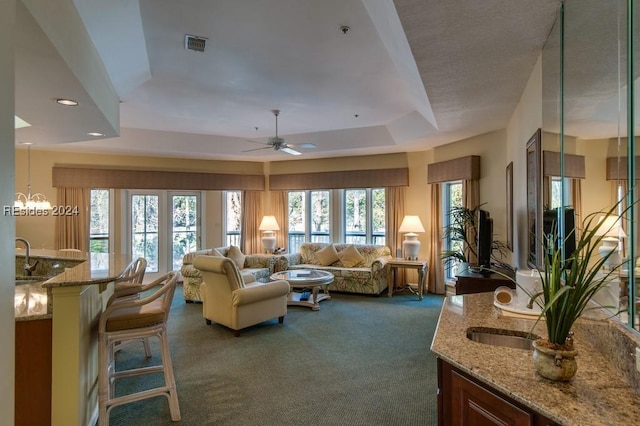 living room with dark colored carpet, a wealth of natural light, ceiling fan, and a tray ceiling