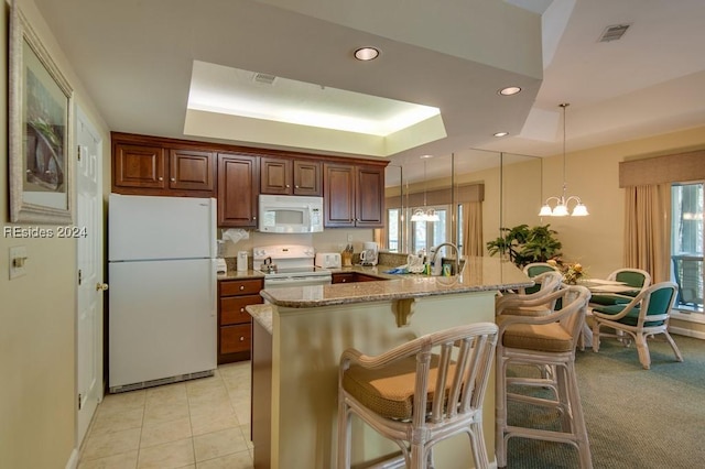 kitchen with decorative light fixtures, a kitchen breakfast bar, a raised ceiling, white appliances, and light stone countertops