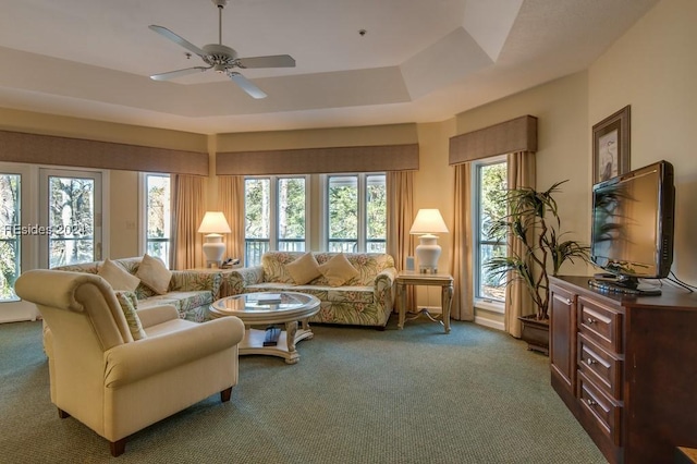 living room with dark carpet, a wealth of natural light, a raised ceiling, and ceiling fan